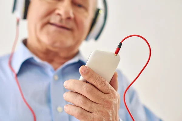 Ηλικιωμένος άνθρωπος ακούγοντας μουσική κρατώντας το τηλέφωνο — Φωτογραφία Αρχείου