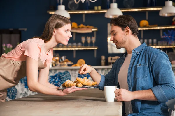 Bom garçom dando croissant para seu cliente — Fotografia de Stock