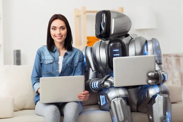 Pleasant girl sitting on the couch with robot — Stock Photo, Image