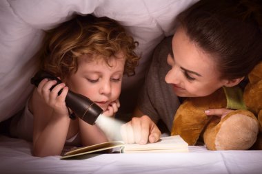 Mother and son reading book under blanket clipart