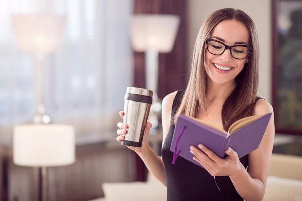 Woman looking at notebook and holding thermo mug — Stockfoto