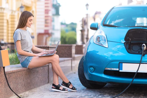 Vrouw met behulp van de laptop tijdens het opladen van de auto — Stockfoto