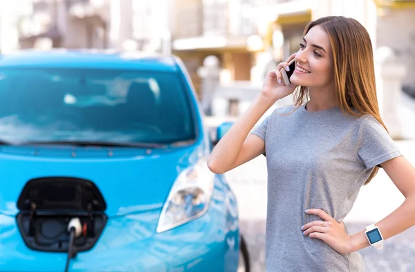 Frau telefoniert mit Smartphone, während sie Auto lädt — Stockfoto