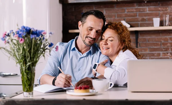 Frau kuschelt Mann während er in Küche sitzt — Stockfoto