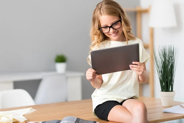 Chica sentada en la mesa y sosteniendo la tableta — Foto de Stock