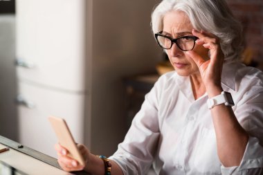 Yaşlı kadın telefonunda yeni iletiyi alan endişeli