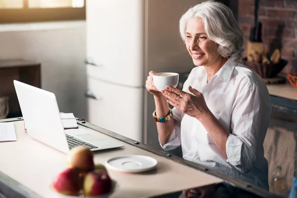 Erderly woman using computer while enjoying her coffee — Stock Photo, Image