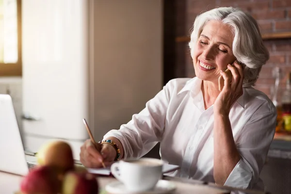 Oude vrouw praten over de telefoon terwijl het maken van notities — Stockfoto