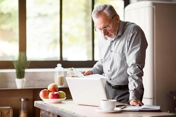 Senior man controleren zijn papieren in keuken thuis — Stockfoto