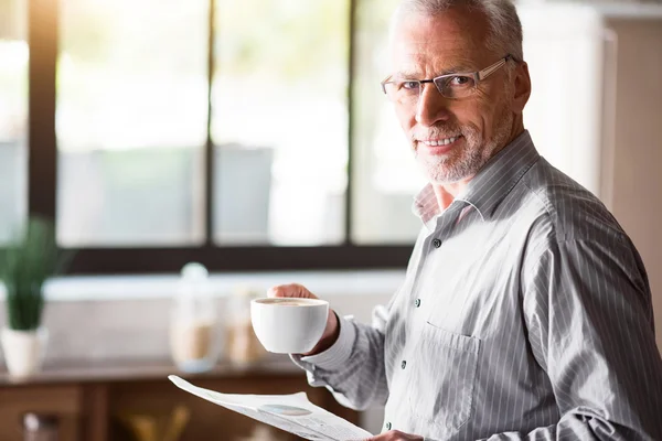 Viejo sonriendo mientras sostiene una taza de café y papel — Foto de Stock