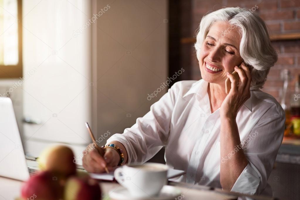 Old woman talking on the phone while taking notes