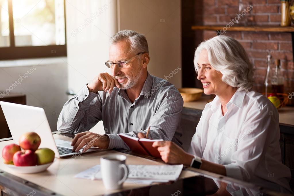 Happy senior couple using laptop at the kitchen