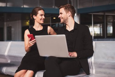 Havaalanında bilgisayar kullanan gülümseyen bir adam ve kadın.