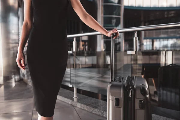 Femme portant une robe noire et tenant une valise pratique — Photo