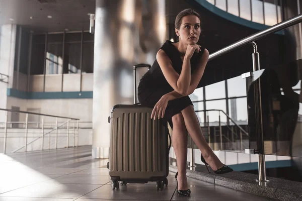 Kobieta siedząca na walizce czekając na lot — Zdjęcie stockowe