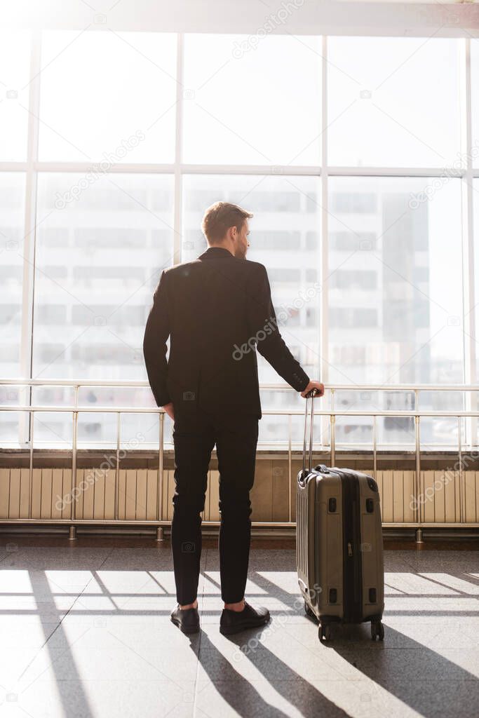 Man standing with a suitcase near the huge window