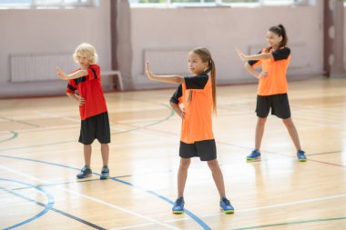 Spor salonunda egzersiz yapan ve sağa dönen üç çocuk.