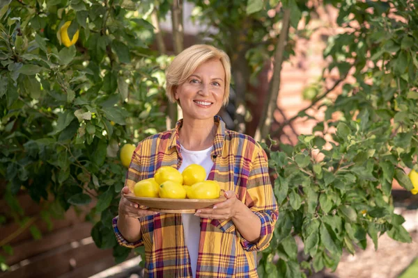Улыбающаяся блондинка держит тарелку с лимонами в саду — стоковое фото