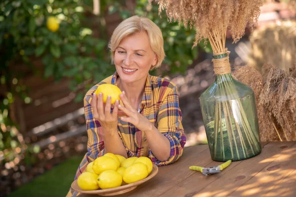 ブロンドの女性は庭の木製のテーブルに座ってレモンを持って — ストック写真
