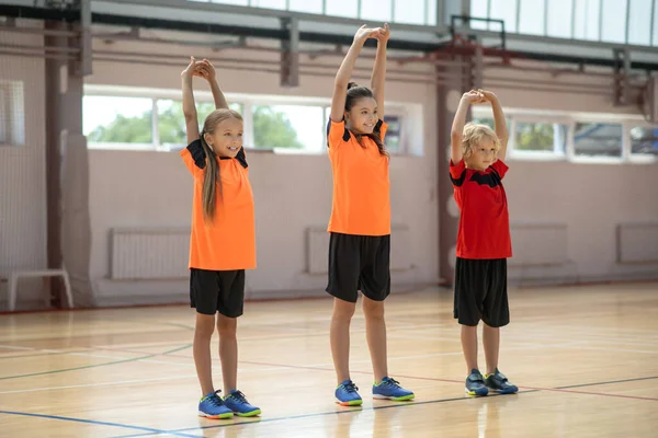 Tres niños haciendo estiramiento en PE lección — Foto de Stock