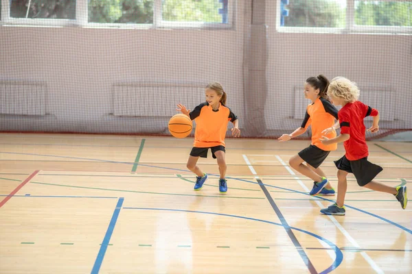 Kinder in heller Sportbekleidung spielen gemeinsam Basketball und fühlen sich energiegeladen — Stockfoto