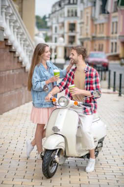 Kadın ve erkek mobilet sürerken kahve molası veriyorlar.