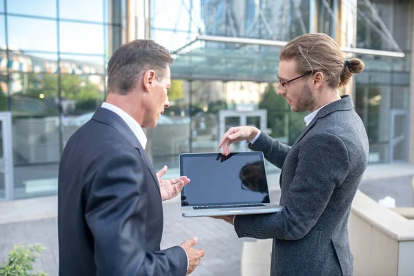 ノートパソコンの外に立ってビジネスの問題を議論する2人の男性の同僚 — ストック写真