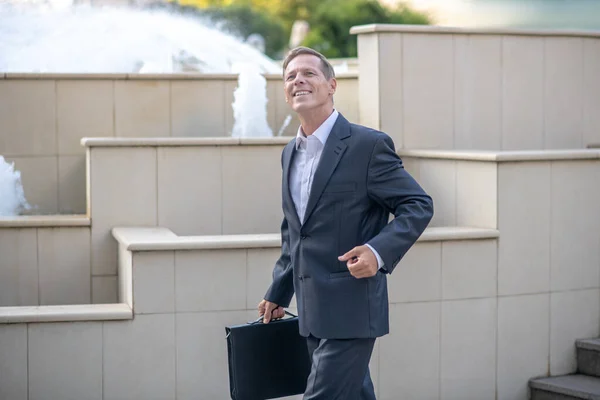 Glimlachende volwassen zakenman lopen met zaak naar beneden de trap buiten — Stockfoto