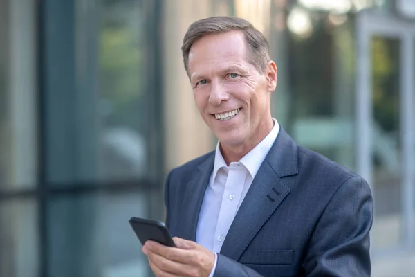 Glimlachende volwassen zakenman controleren van zijn telefoon buiten — Stockfoto