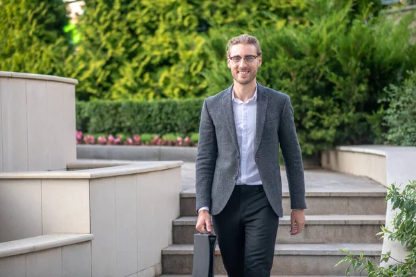 Leende manlig kontorsarbetare går ner för trappor utanför, bärande väska — Stockfoto