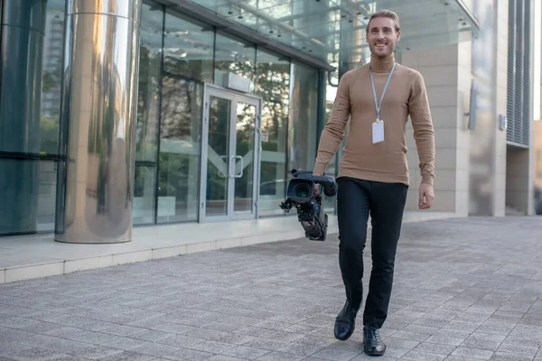 운전자가 오른쪽 손에 카메라를 들고 현대식 건물 앞을 걷고 있다 — 스톡 사진
