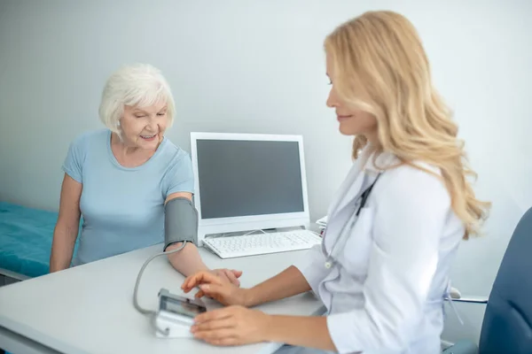 Cardiologista do sexo feminino medindo a pressão arterial para a mulher idosa bonita — Fotografia de Stock