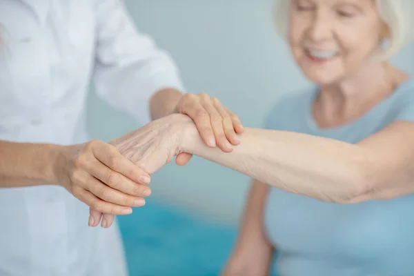 Médico examinando la muñeca de una anciana sonriente — Foto de Stock