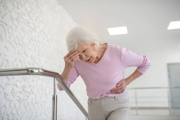 Mujer anciana con una camisa rosa que sufre de dolor de cabeza — Foto de Stock