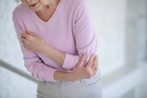 Oudere vrouw in roze shirt lijdt aan pijn in de elleboog — Stockfoto