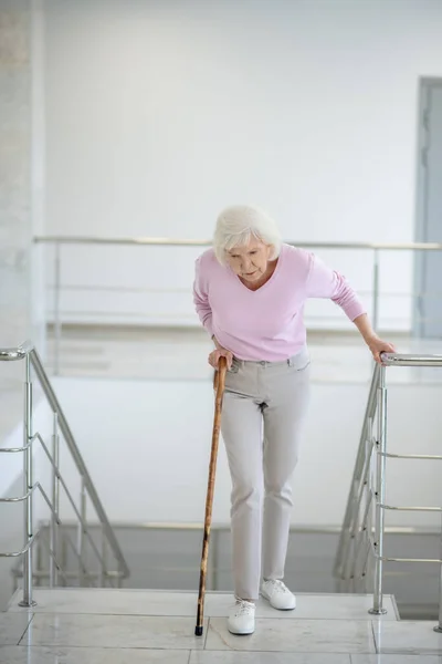 Oudere vrouw met een wandelstok die naar beneden gaat en er moe uitziet — Stockfoto