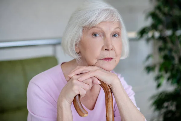 Grijsharige vrouw met wandelstok die er serieus en attent uitziet — Stockfoto