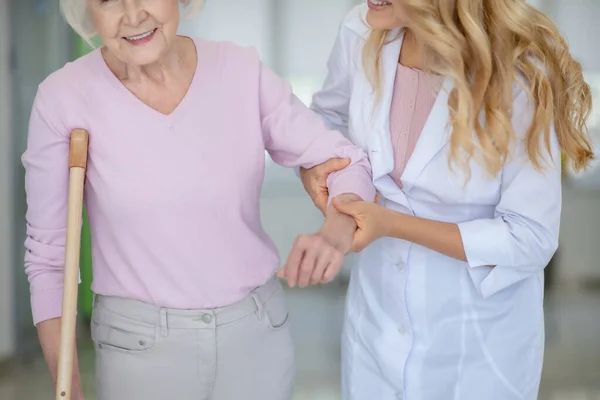 Pielęgniarka wspierająca starszą kobietę w różowej koszuli — Zdjęcie stockowe