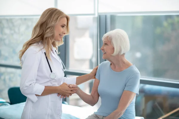 Enfermeira sorridente bonito de cabelos compridos falando com um paciente idoso — Fotografia de Stock