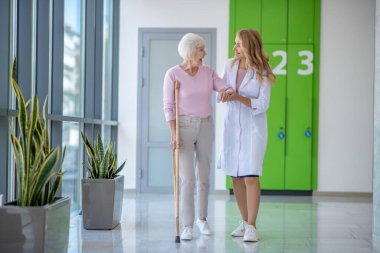 Laboratuvar önlüklü bir doktor ve birlikte yürüyen bir hasta.