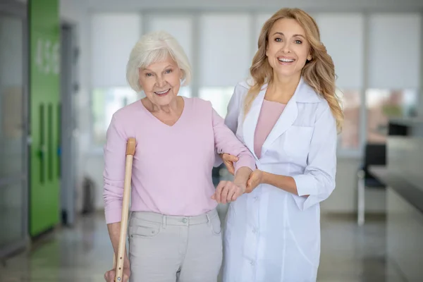 Dokter in een labjas ondersteunt haar patiënt en beide lachend — Stockfoto