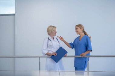 İki kadın doktor merdiven korkuluklarına yaslanıyor, arkadaşça sohbet ediyorlar.