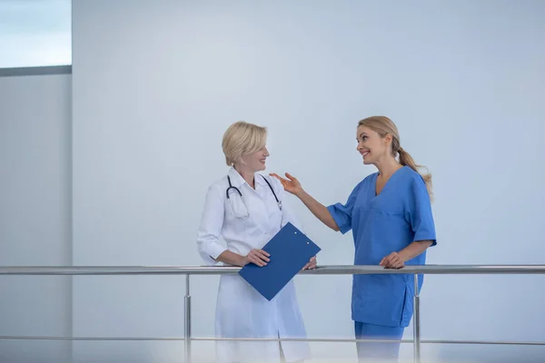 Две женщины-доктора, опирающиеся на перила лестницы, дружелюбно беседуют — стоковое фото
