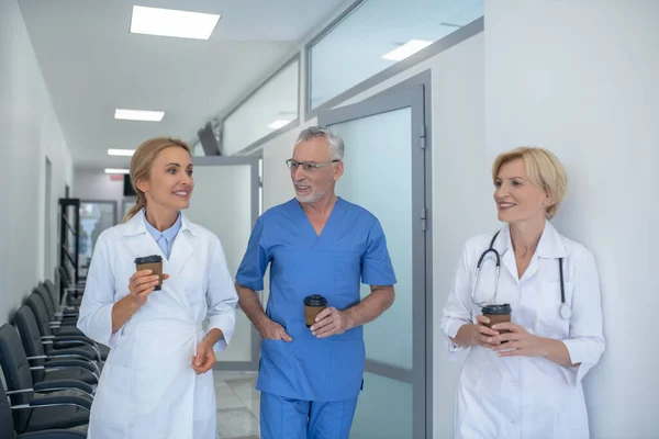 Group of smiling doctors enjoying coffee in the corridor