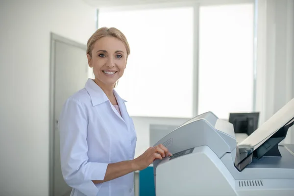 Justo cabelo jovem médico olhando ocupado no trabalho e sorrindo — Fotografia de Stock