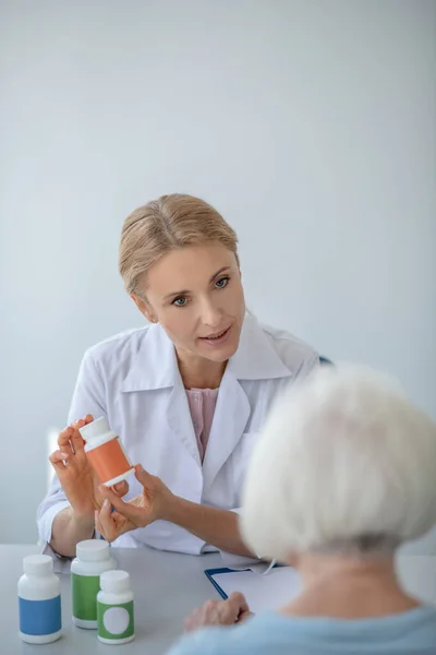Médico femenino recetando medicamentos a pacientes de edad avanzada y mirando implicado — Foto de Stock