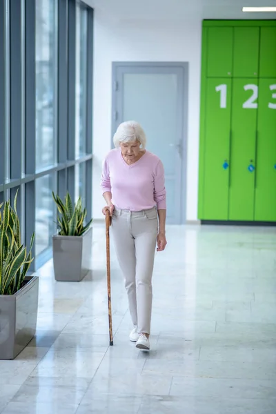 Koridorda yürüyen bastonlu gri saçlı kadın. — Stok fotoğraf