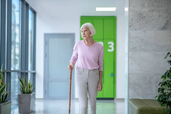 Koridorda yürüyen bastonlu gri saçlı kadın. — Stok fotoğraf