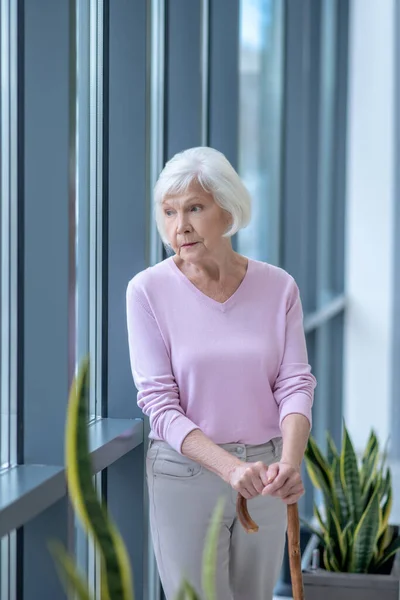 Mujer de pelo gris con un bastón de pie y aspecto reflexivo — Foto de Stock