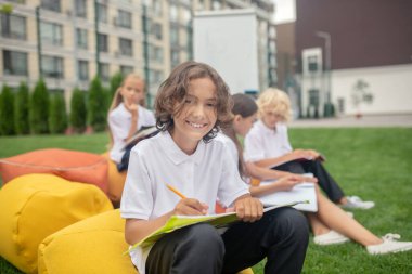 Koyu saçlı, beyaz tişörtlü, mutlu görünen bir öğrenci.